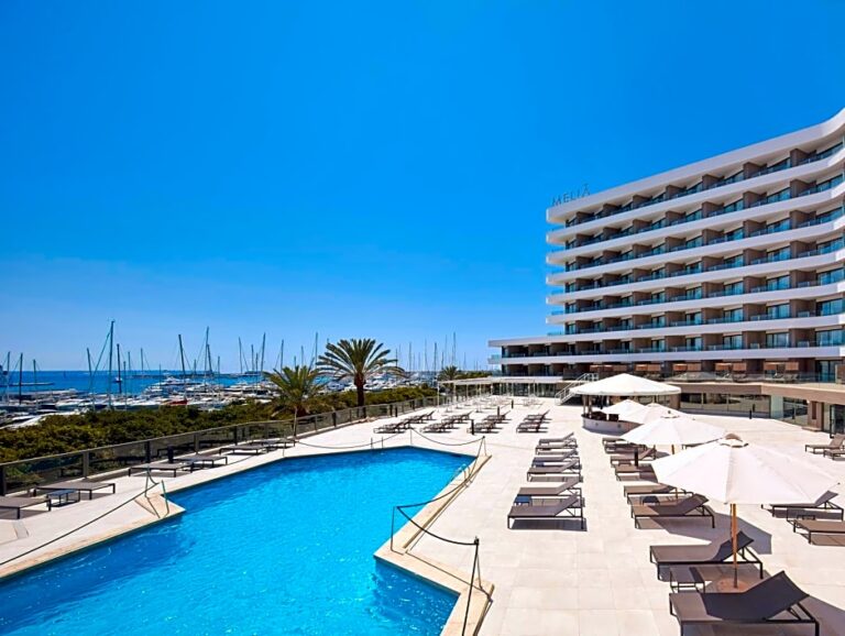 A Pool With Umbrellas And Chairs By A Building