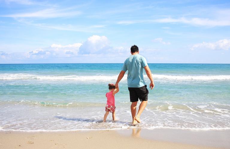 A Man And Child Walking On A Beach
